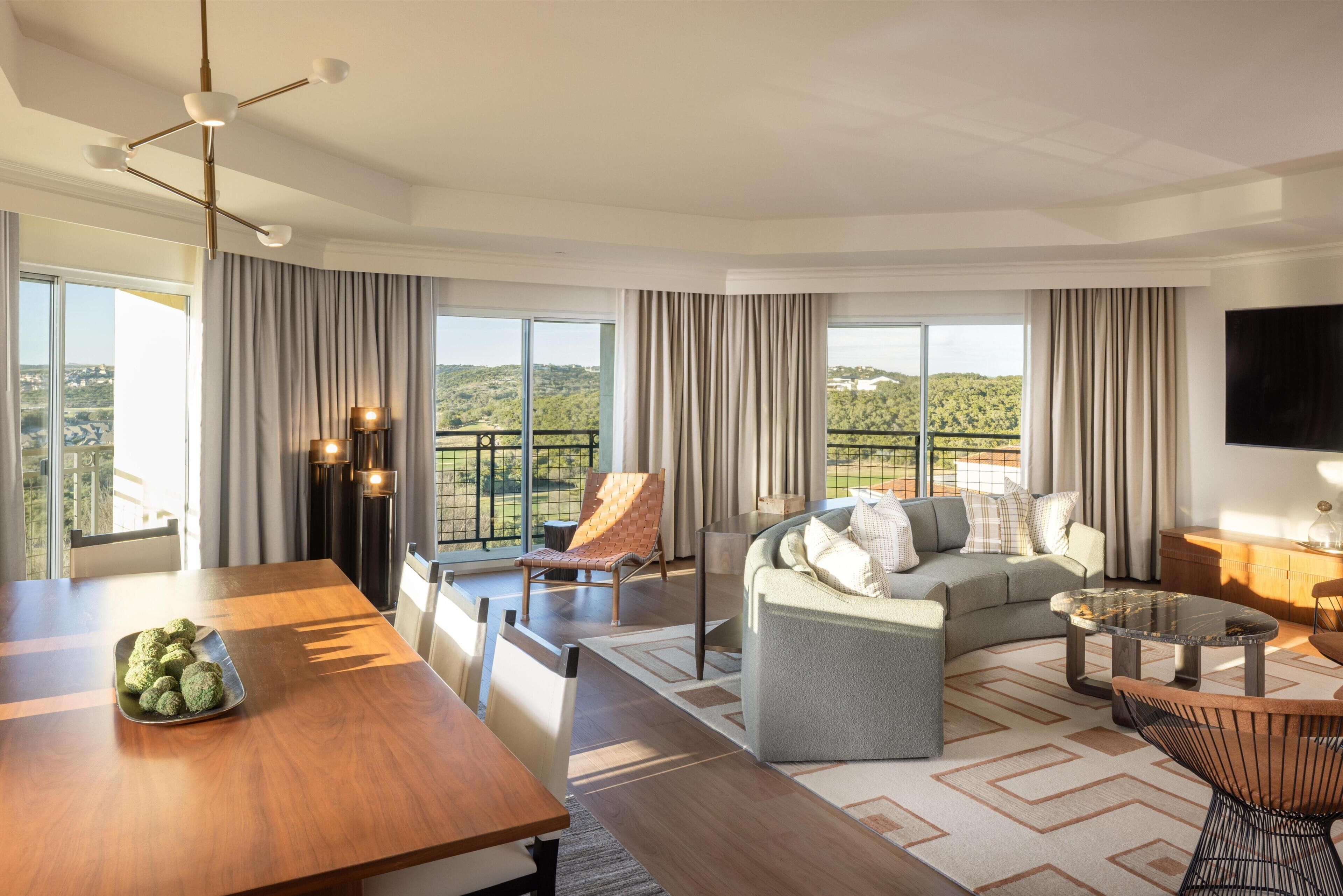 A modern living room with a sofa, a dining table, and a balcony with a view.