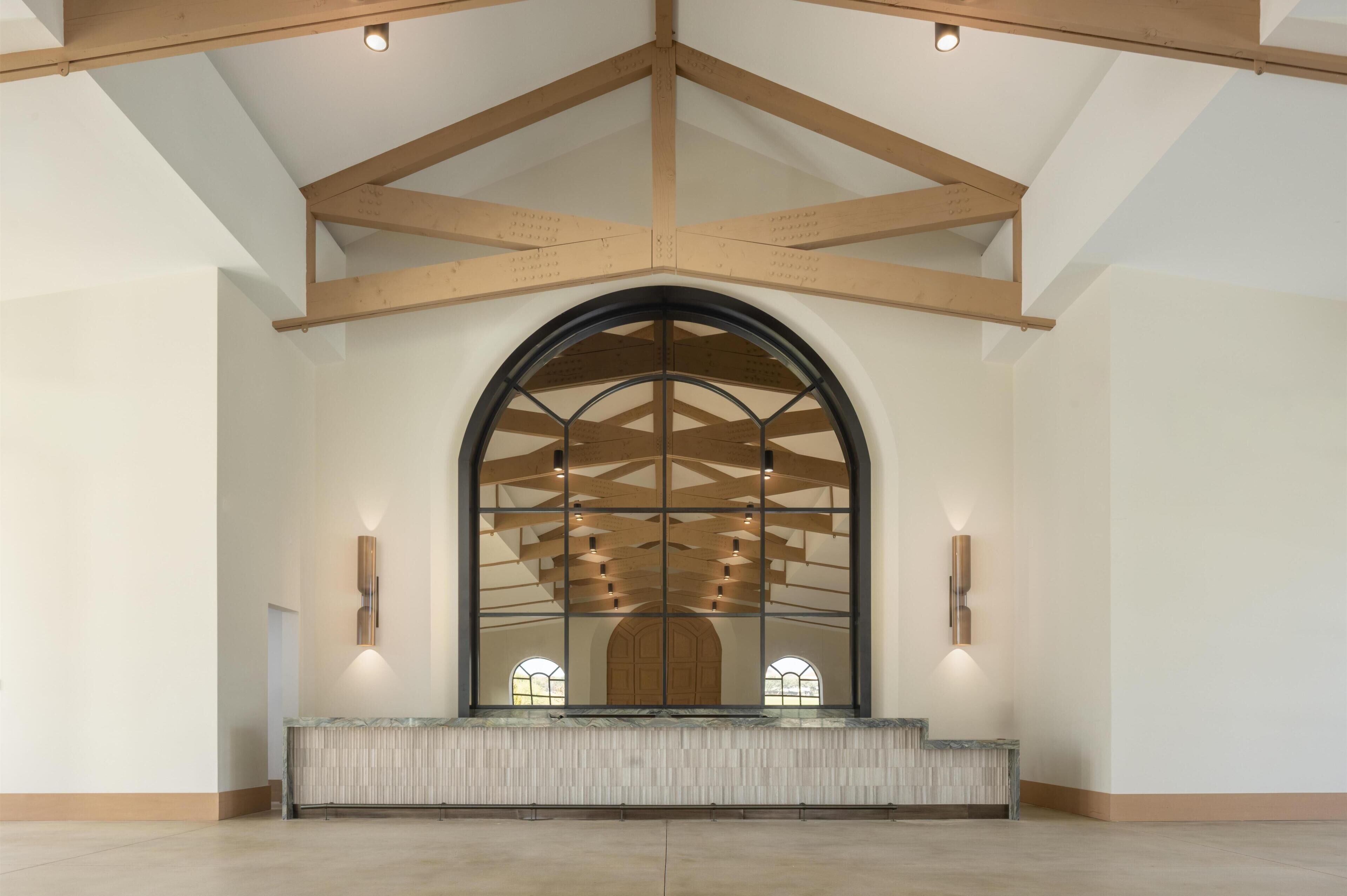 A spacious interior with a high arched window, wooden beams, and a marble bench.