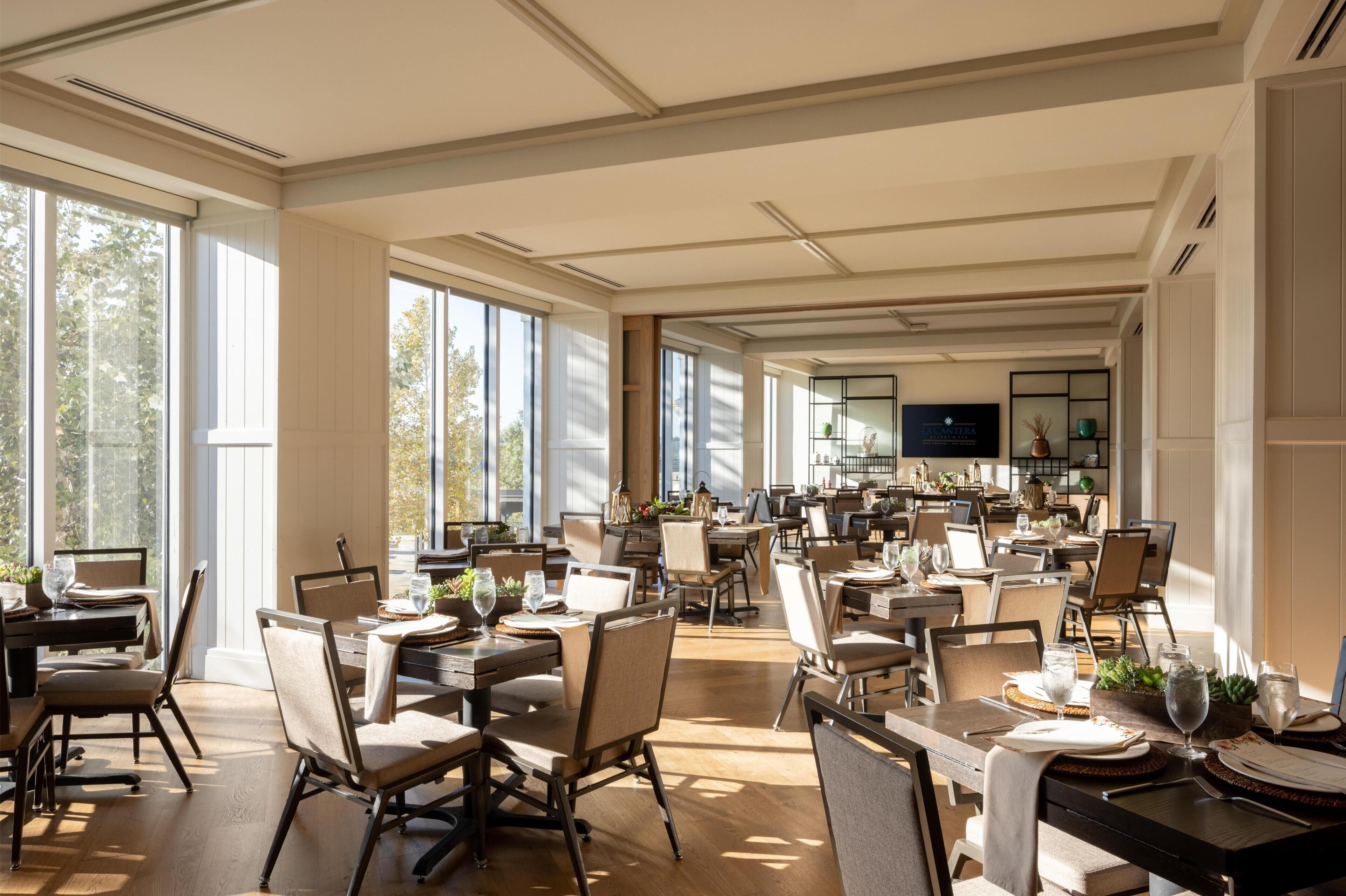Un comedor amplio con varias mesas y sillas, ventanas grandes y un diseño interior moderno.
