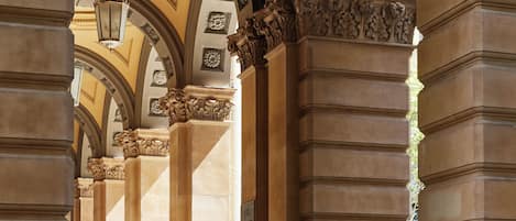 An architectural corridor with ornate columns, a chandelier, and a tiled floor.