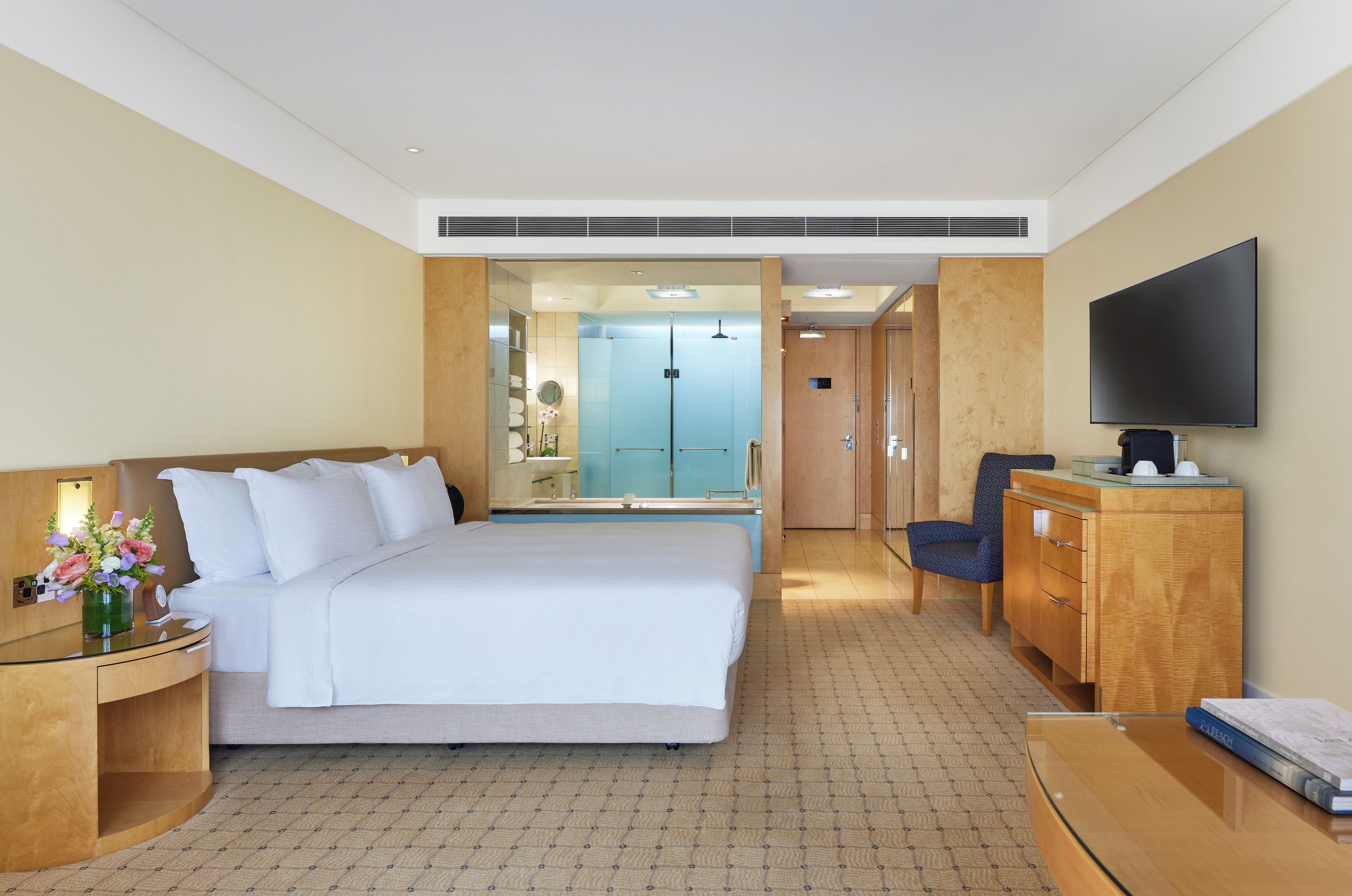 A hotel room with a large bed, a desk with a flat-screen TV, a wooden dresser, and a bathroom visible through an open door.