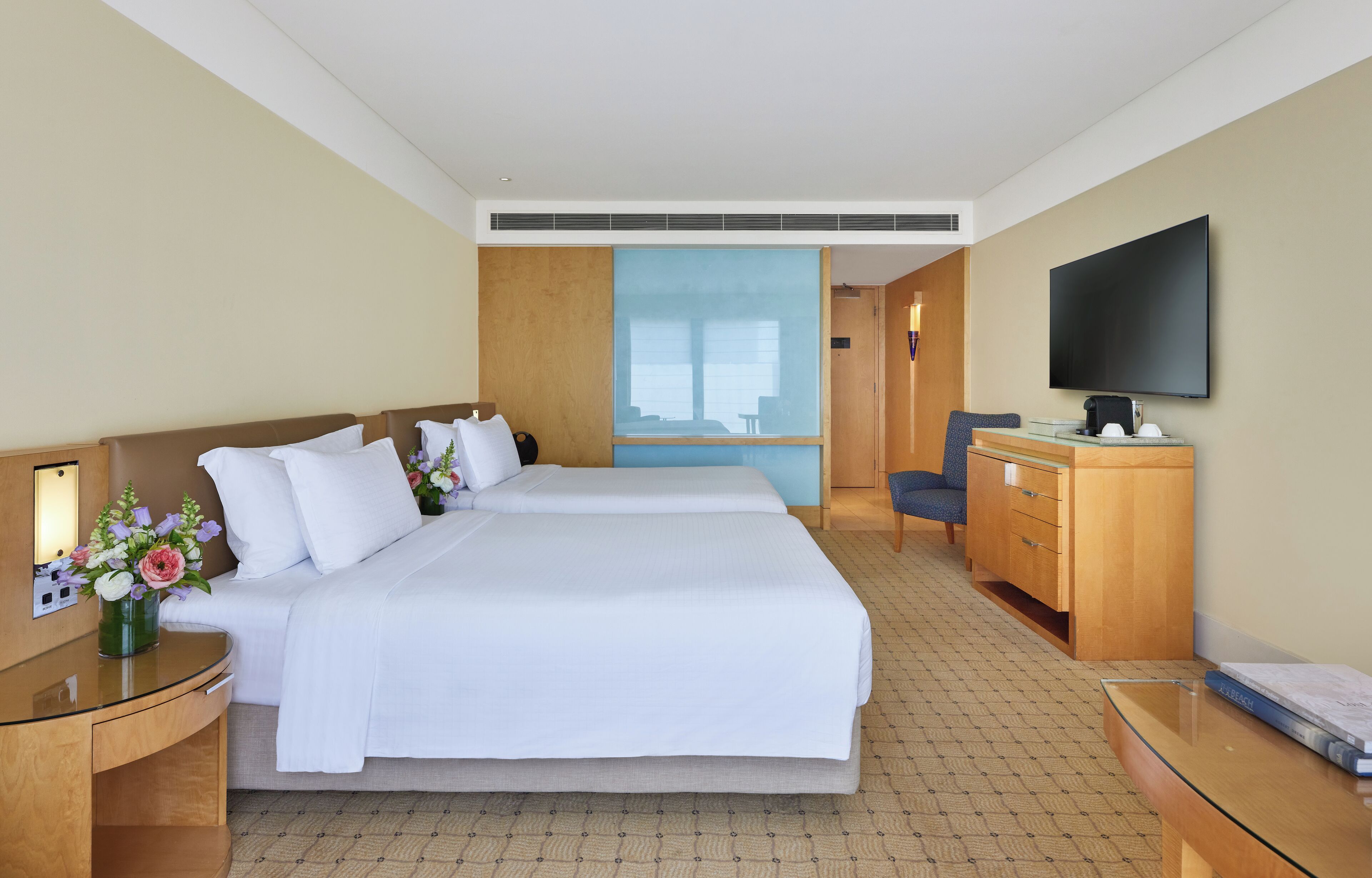 A hotel room with a large bed, a desk with a flat-screen TV, a wooden dresser, and a nightstand with a lamp.