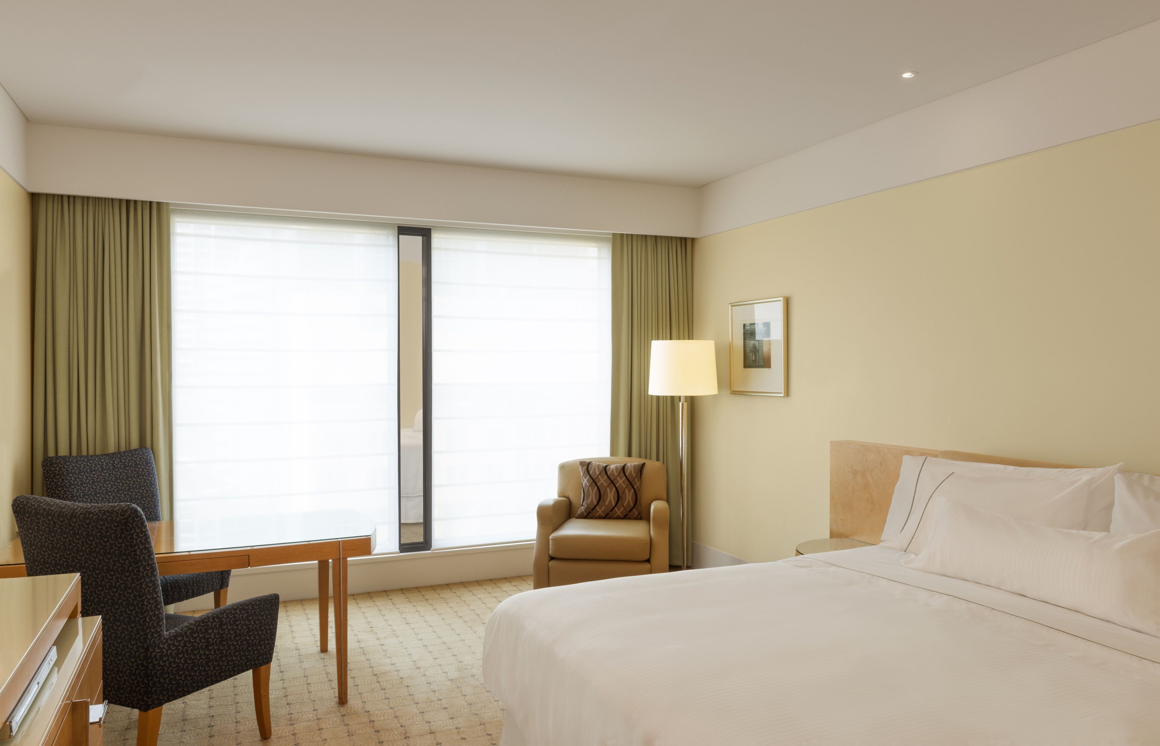 A hotel room with a bed, a desk, two chairs, a lamp, and a window with curtains.