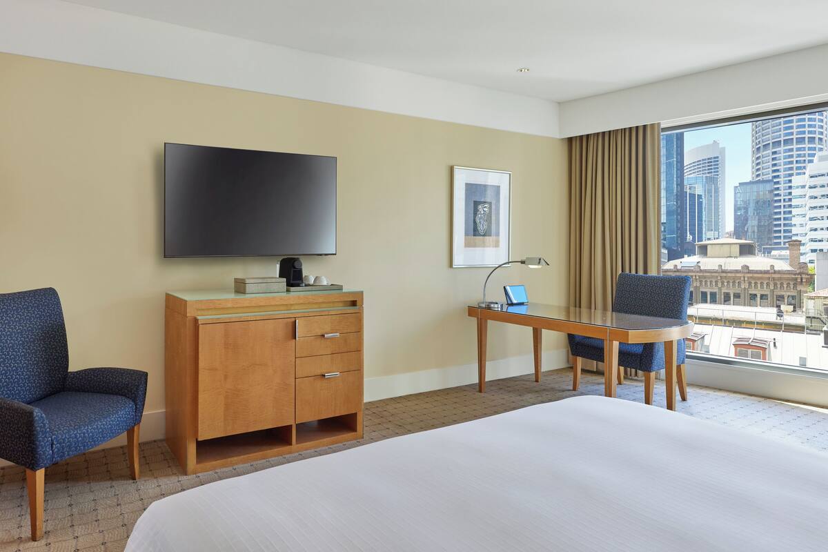 A hotel room with a large bed, a desk with a laptop, a TV, a wooden dresser, and a chair.