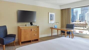 A hotel room with a large bed, a desk with a laptop, a TV, a wooden dresser, and a chair.