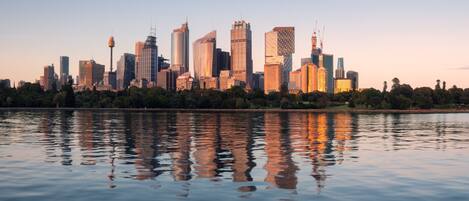 A city skyline reflected in calm water, featuring modern high-rise buildings and a prominent tower.