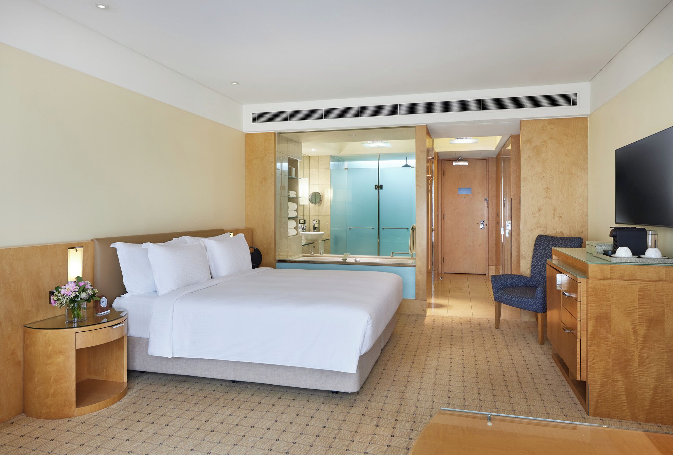 A hotel room with a bed, a desk, a chair, a TV, and a bathroom visible through an open door.