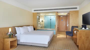 A hotel room with a bed, a desk, a chair, a TV, and a bathroom visible through an open door.