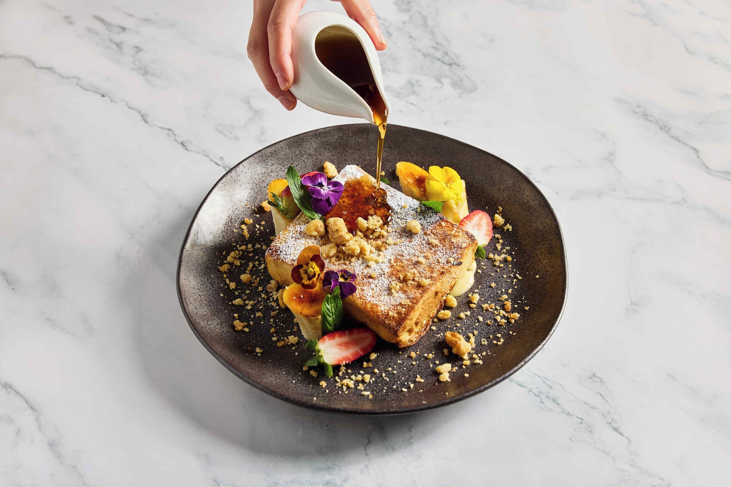 A dessert plate with a piece of toast, fruit, and powdered sugar.