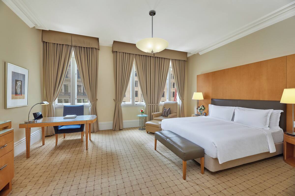 Ein Hotelzimmer mit einem großen Bett, einem Schreibtisch, einem Stuhl und einem kleinen Tisch mit einer Lampe.