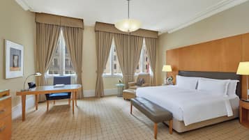 Una habitación de hotel con una cama grande, un escritorio, una silla y una mesita de noche con lámpara.