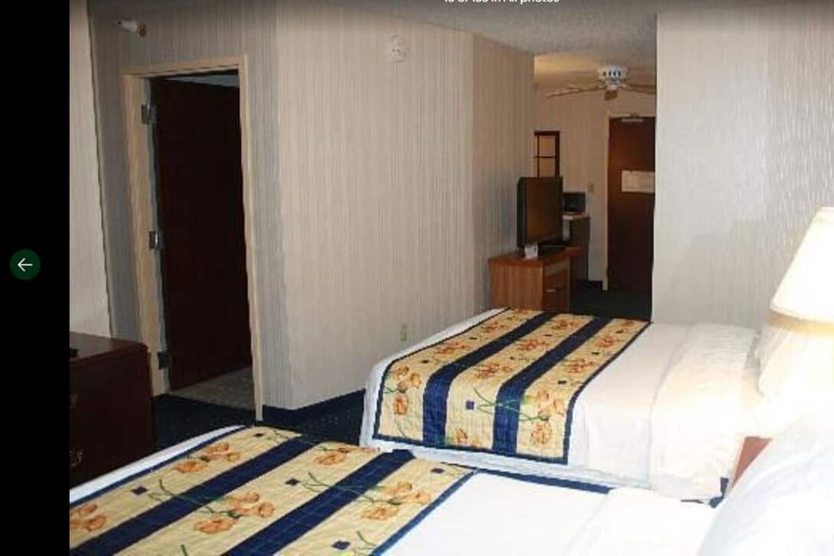 A hotel room with a bed, a desk, a chair, a lamp, and a television.