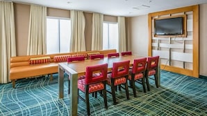 Un salón de conferencias con una mesa larga, sillas rojas, un sofá y un televisor montado en un panel de madera.