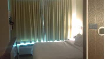 Habitación de hotel con una cama, cortinas, un escritorio y una pared con un diseño de árbol.