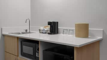 Una cocina compacta con un lavamanos, cafetera y dos vasos sobre la encimera.