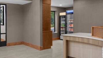A reception area with a wooden reception desk, a glass door leading outside, and a refrigerator stocked with beverages.