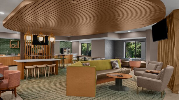 En moderne hotellobby med et centralt siddeområde, en bar og et tv.