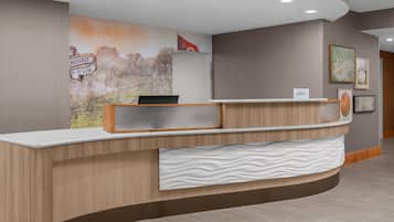 A reception desk with a wooden finish, a white textured panel below it, and a wall mural depicting a landscape with a sign that reads "NEHURST EST 1395".