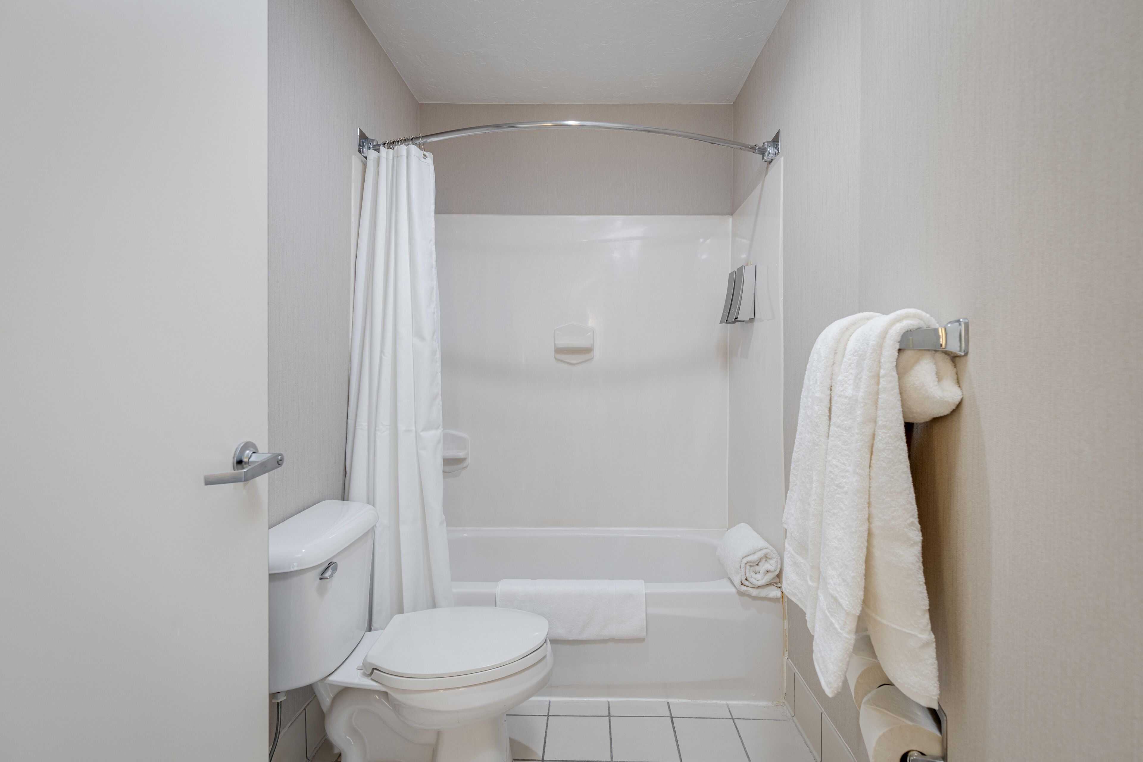 A small, white bathroom with a toilet, shower, and a towel rack.