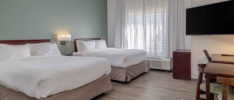 Quarto de hotel com duas camas, televisão, escrivaninha e janela com cortinas.