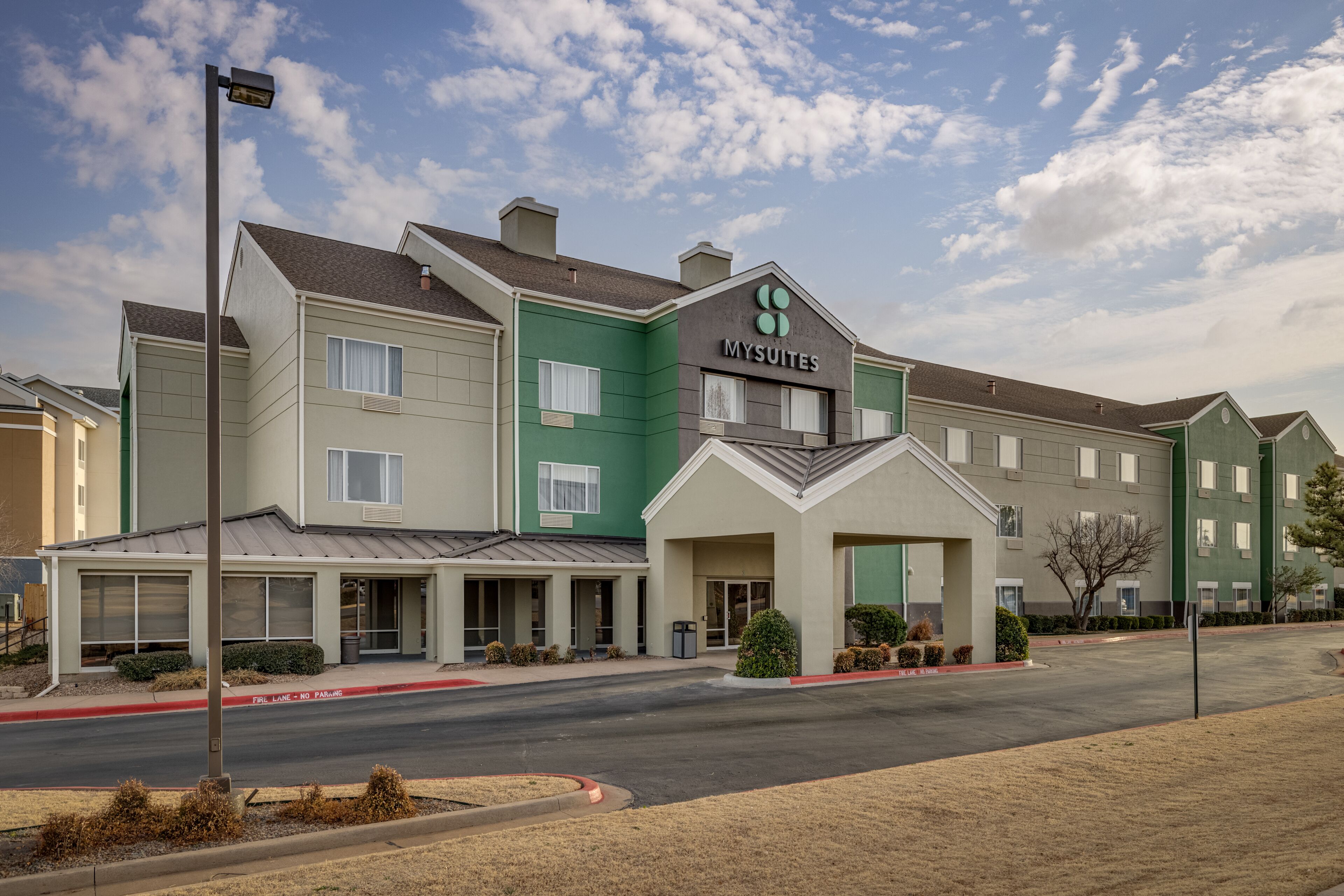 A multi-story hotel with a green and beige facade, a prominent 'MYSUITES' sign, and a covered entrance area.