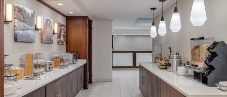 A modern kitchen with a long counter, wooden cabinets, and pendant lighting.