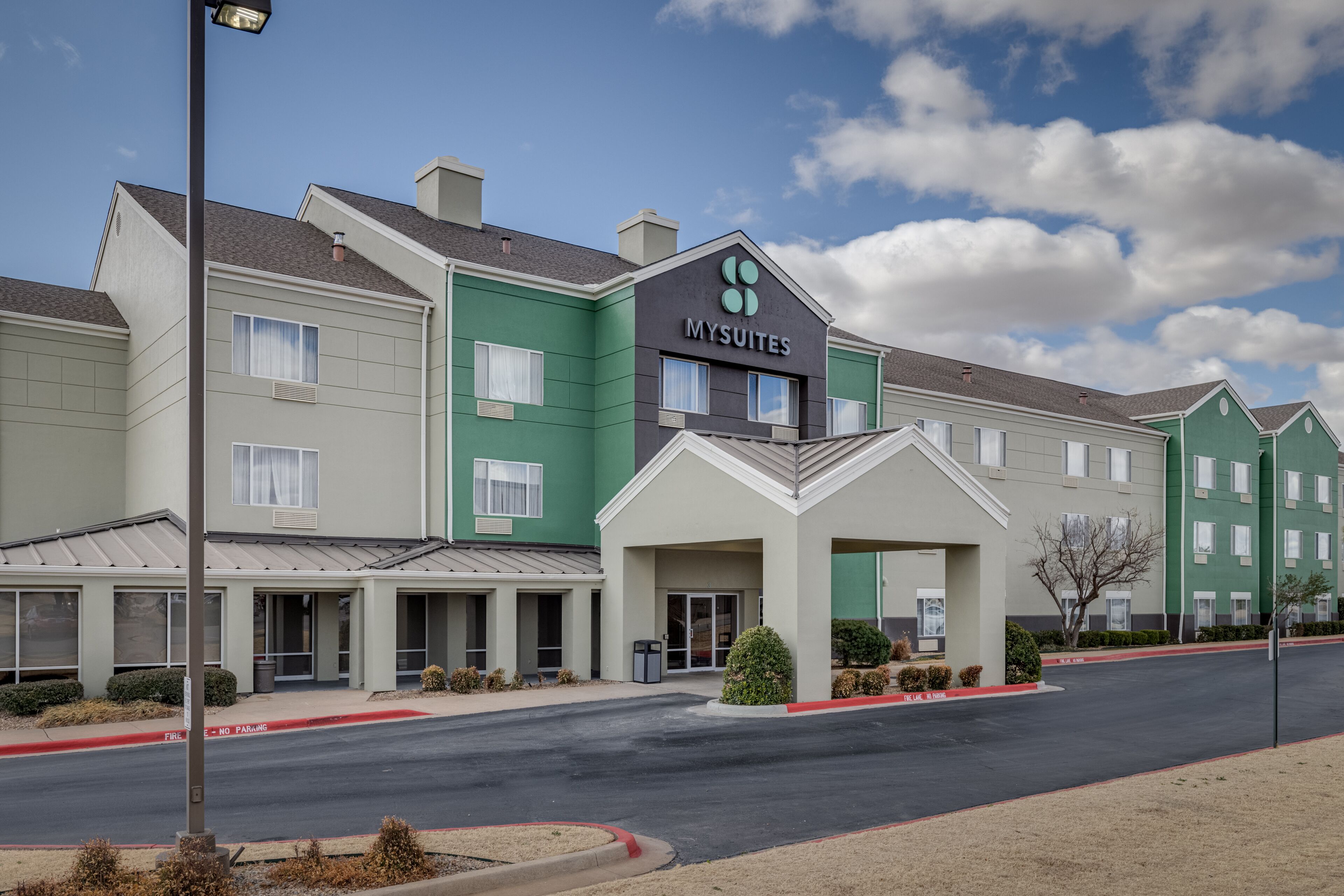 A hotel with a green and beige facade, a covered entrance, and a parking lot.