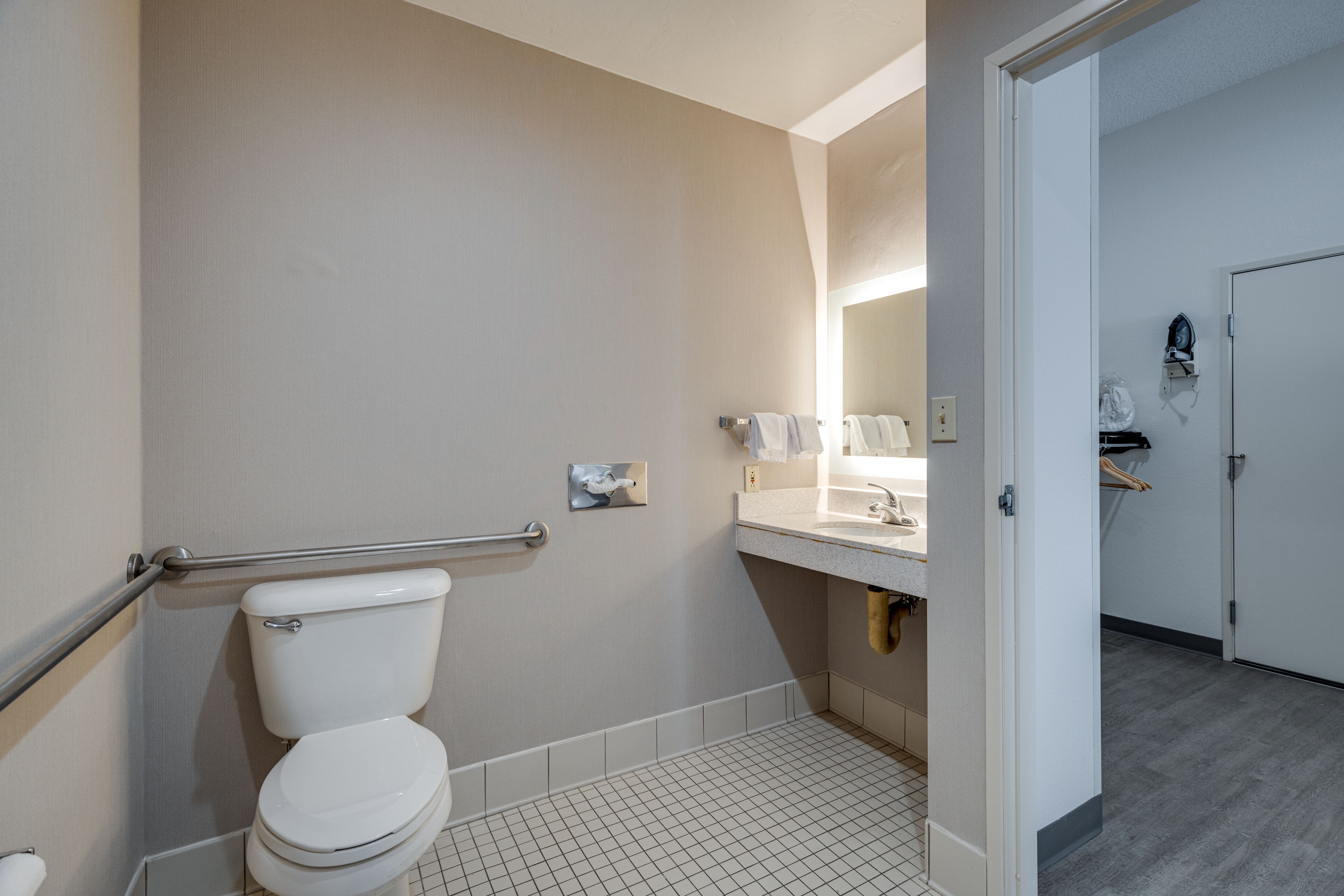 Un baño con inodoro, barra de apoyo, lavamanos y espejo.