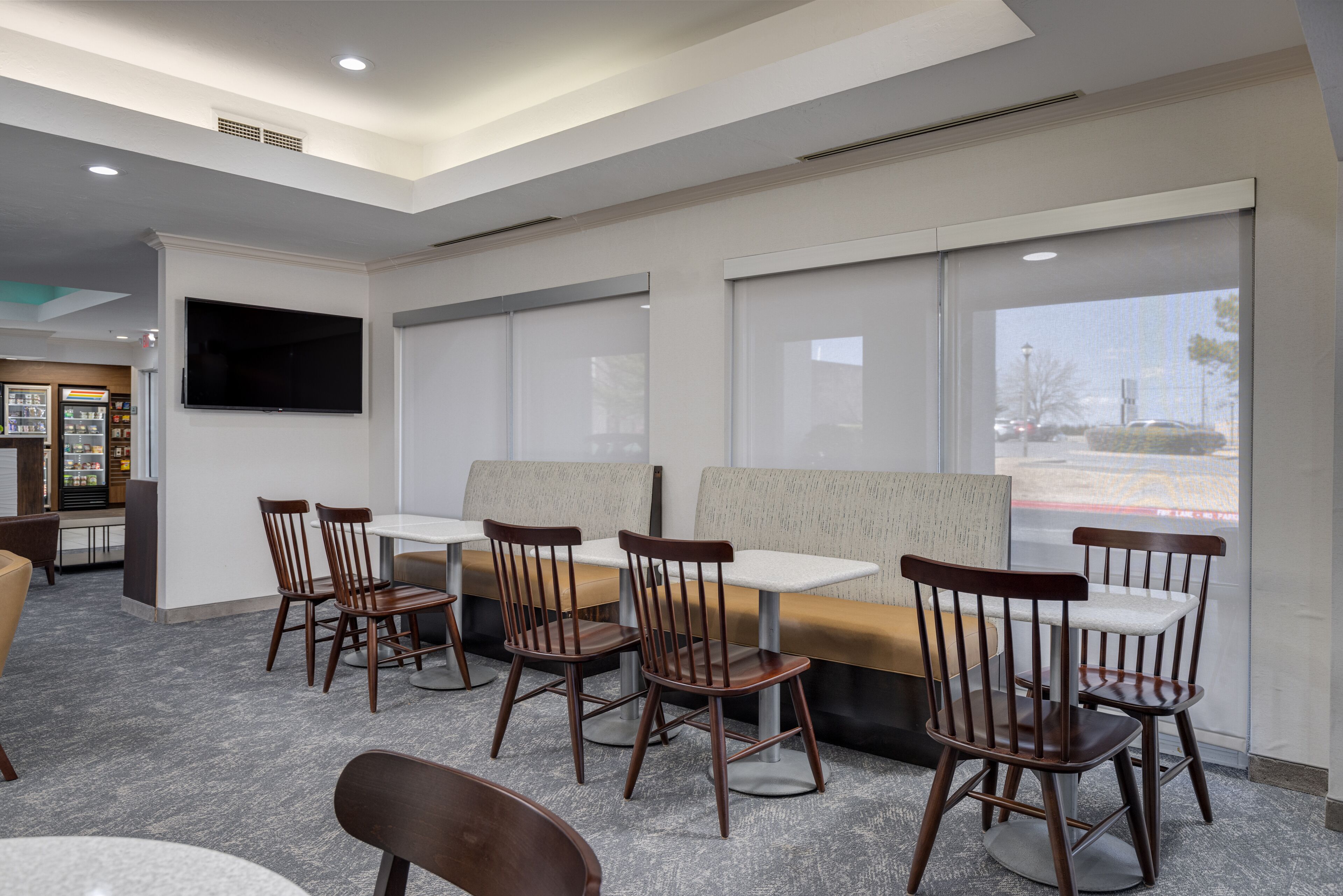 A modern restaurant interior with wooden chairs, cushioned booths, and a large TV screen.