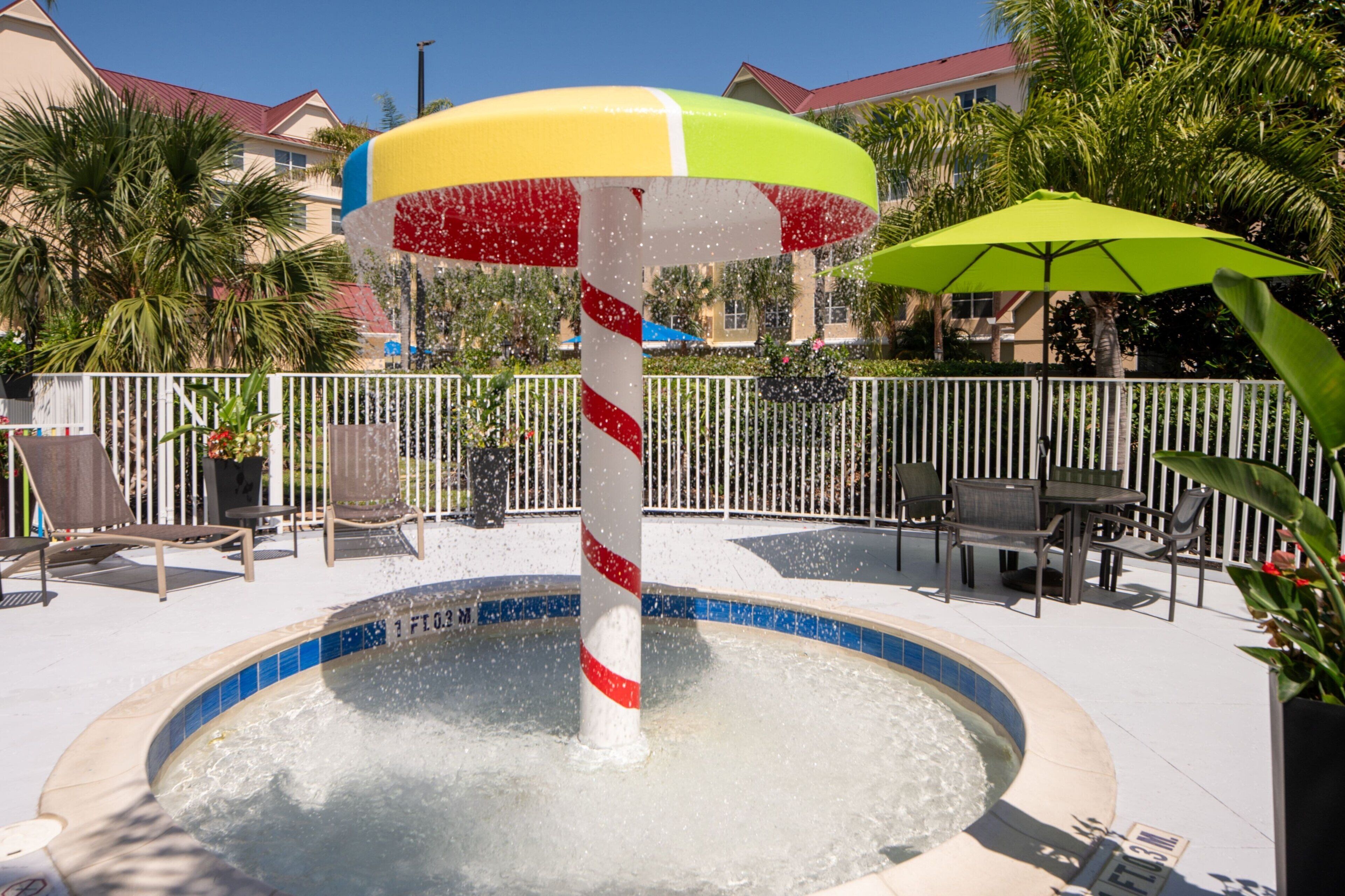 A pool area with a water fountain, lounge chairs, and umbrellas.