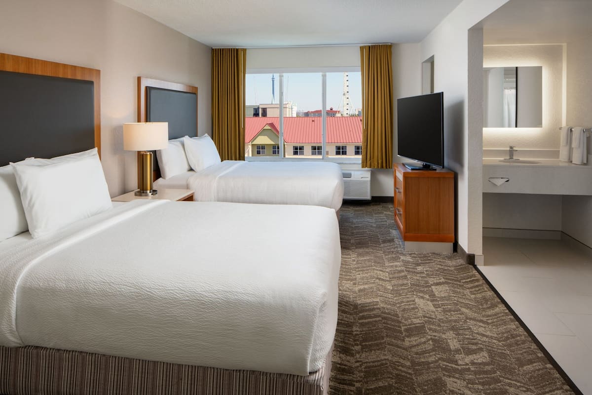 A hotel room with two beds, a TV, a desk, and a bathroom.