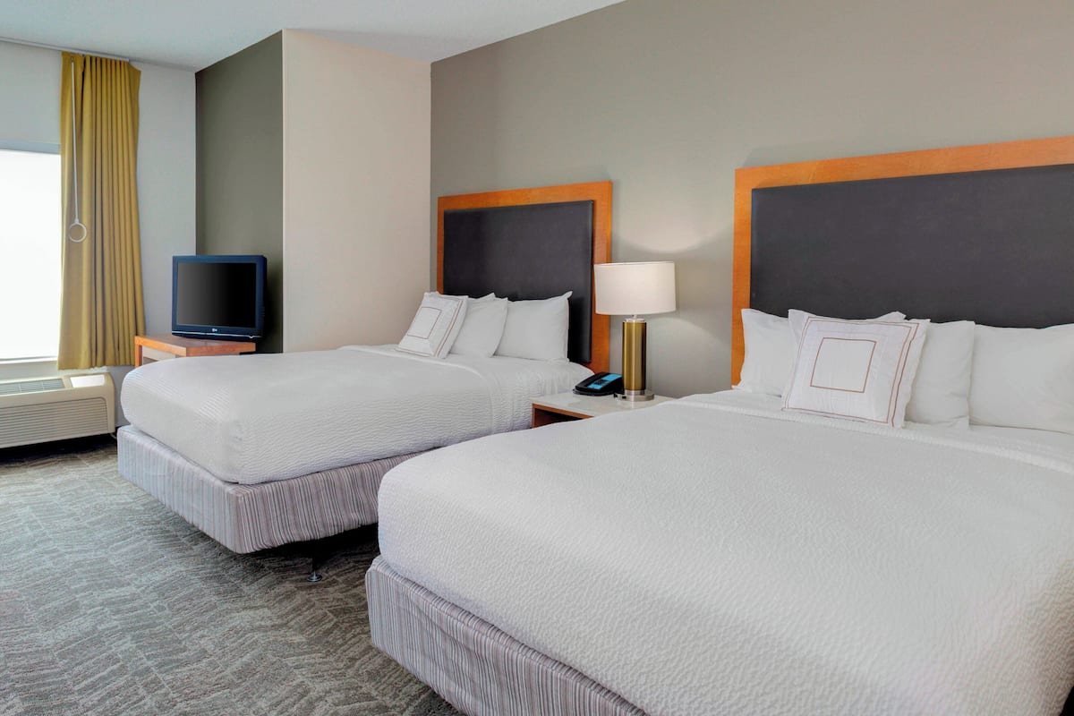 A hotel room with two beds, a television, a lamp, and a bedside table.