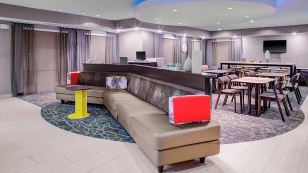 A modern hotel lobby with a curved seating area, a reception desk, and a dining area with multiple tables and chairs. - Springhill Suites Memphis East / Galleria (Memphis)