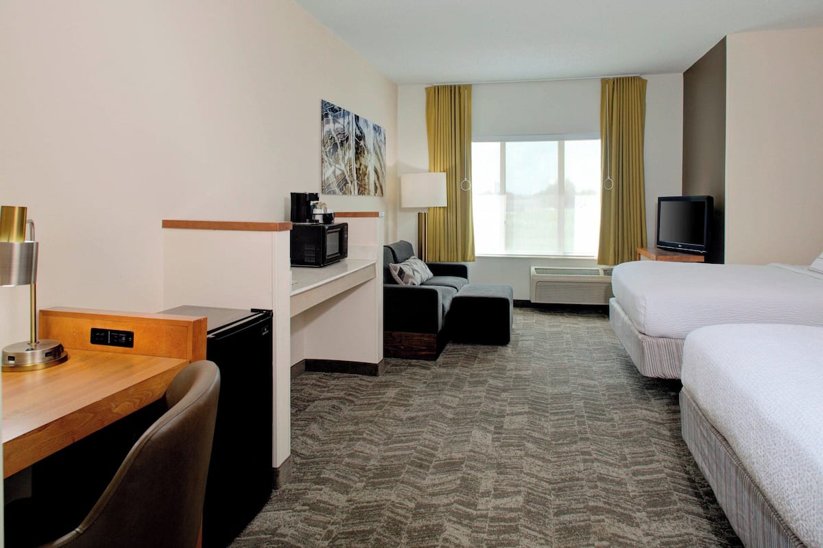 A hotel room with a bed, a desk with a computer, a chair, a sofa, a television, and a window with curtains.