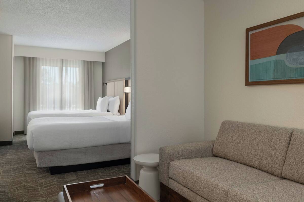 A hotel room with two beds, a sofa, a small table, and a painting on the wall.