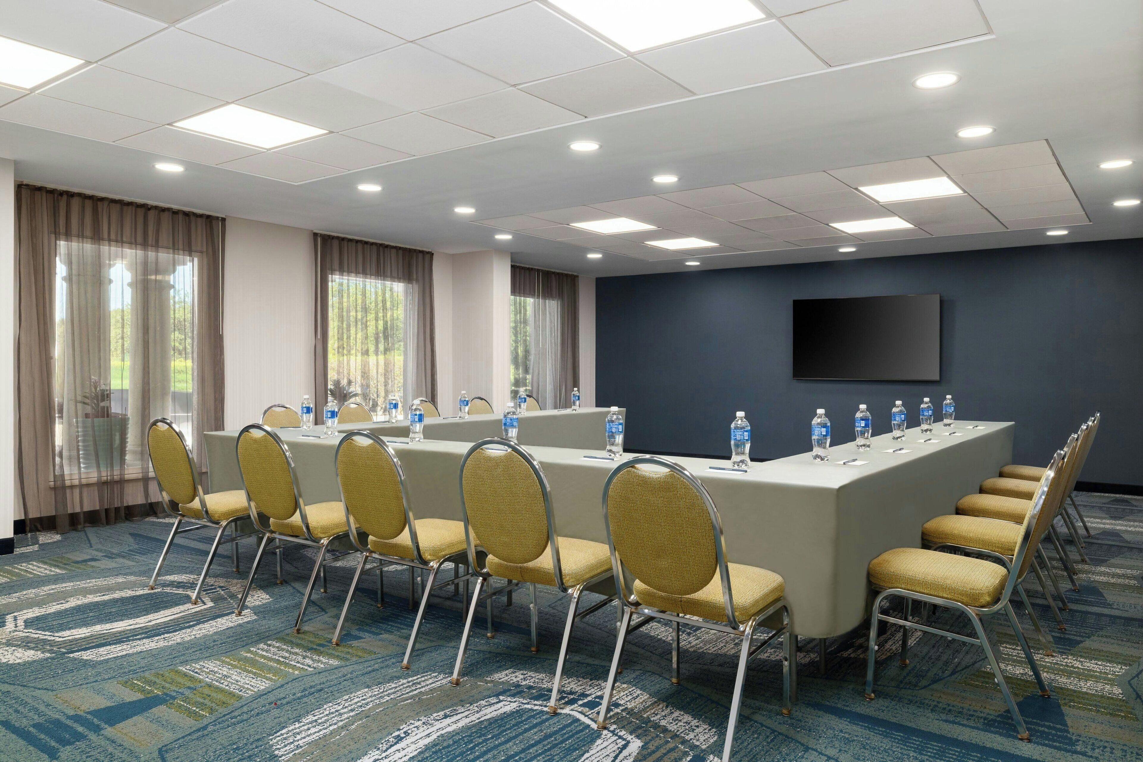 A conference room with a long table, chairs, water bottles, and a flat-screen TV on the wall.