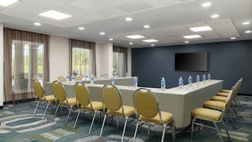A conference room with a long table, chairs, water bottles, and a flat-screen TV on the wall.