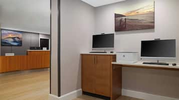 Un área de recepción de hotel moderna con un mostrador de madera, dos monitores y un cuadro grande de una puesta de sol sobre el océano.