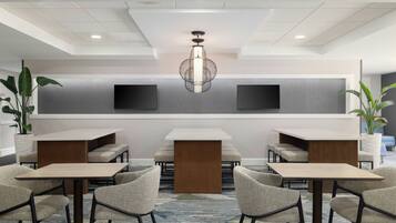Um saguão moderno de hotel com área de estar central, um candelabro grande e duas TVs de tela plana na parede.