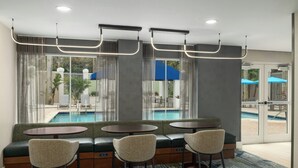 Un espace aménagé avec des sièges au bord de la piscine, offrant une vue sur celle-ci, une porte vitrée donnant sur l’extérieur et un luminaire fixé au plafond.