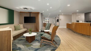 Un hall d’entrée moderne avec un canapé, des fauteuils, un comptoir d’accueil et un téléviseur à écran plat.