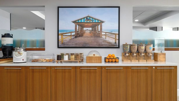 Un comptoir de cuisine avec un bar pour prendre le petit-déjeuner, une machine à café, un présentoir de fruits et un grand tableau encadré représentant une jetée.