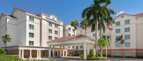 A hotel with a covered entrance, palm trees, and an American flag.