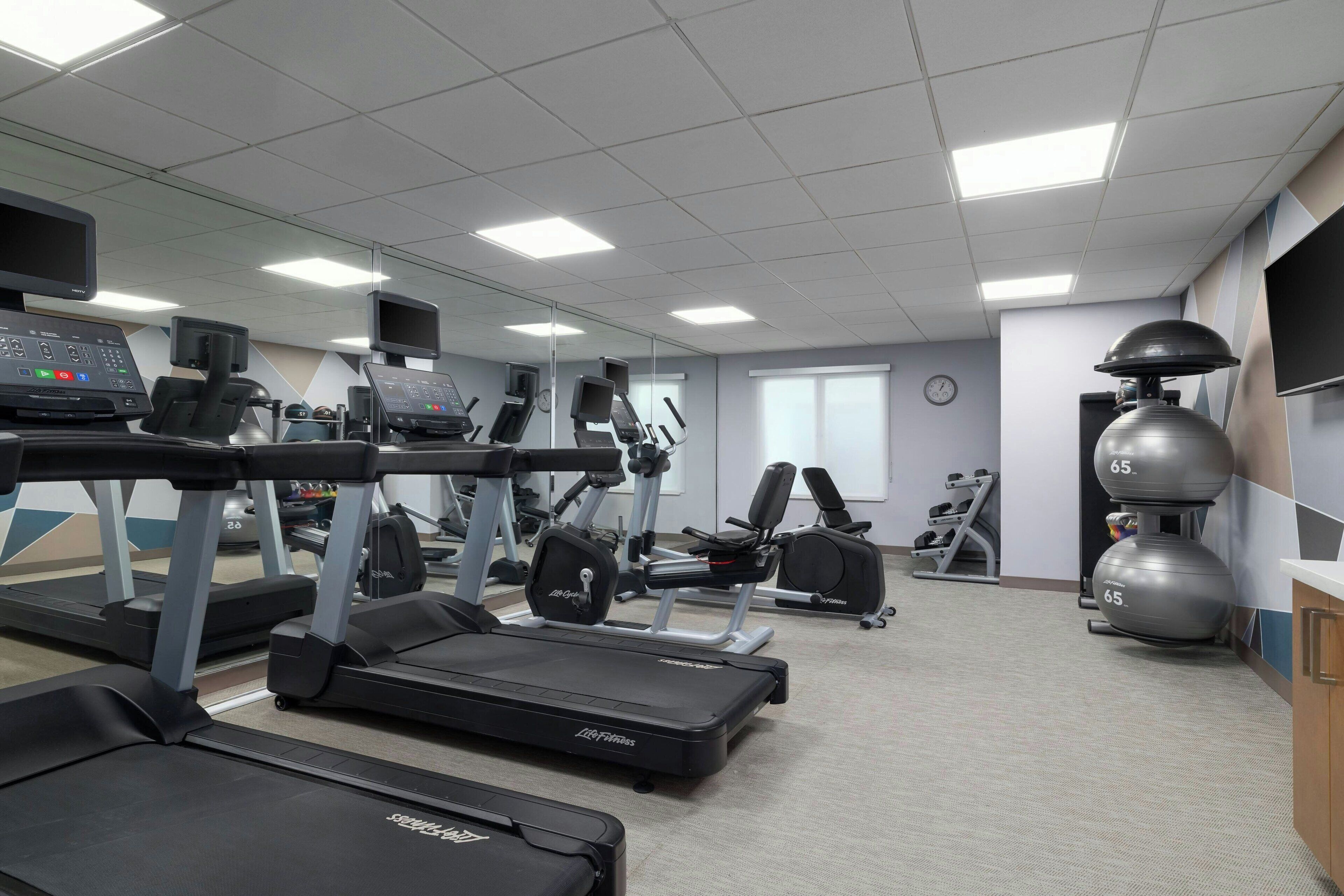 A gym with treadmills, weight machines, and a mirrored wall.