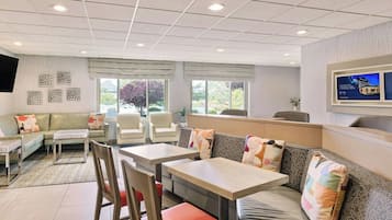 Une chambre d’hôtel moderne équipée d’un canapé, de deux tables, d’une télévision et d’une fenêtre donnant sur un paysage arboré.