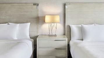 A hotel room with two beds, a nightstand with a lamp, and a small table with a vase.
