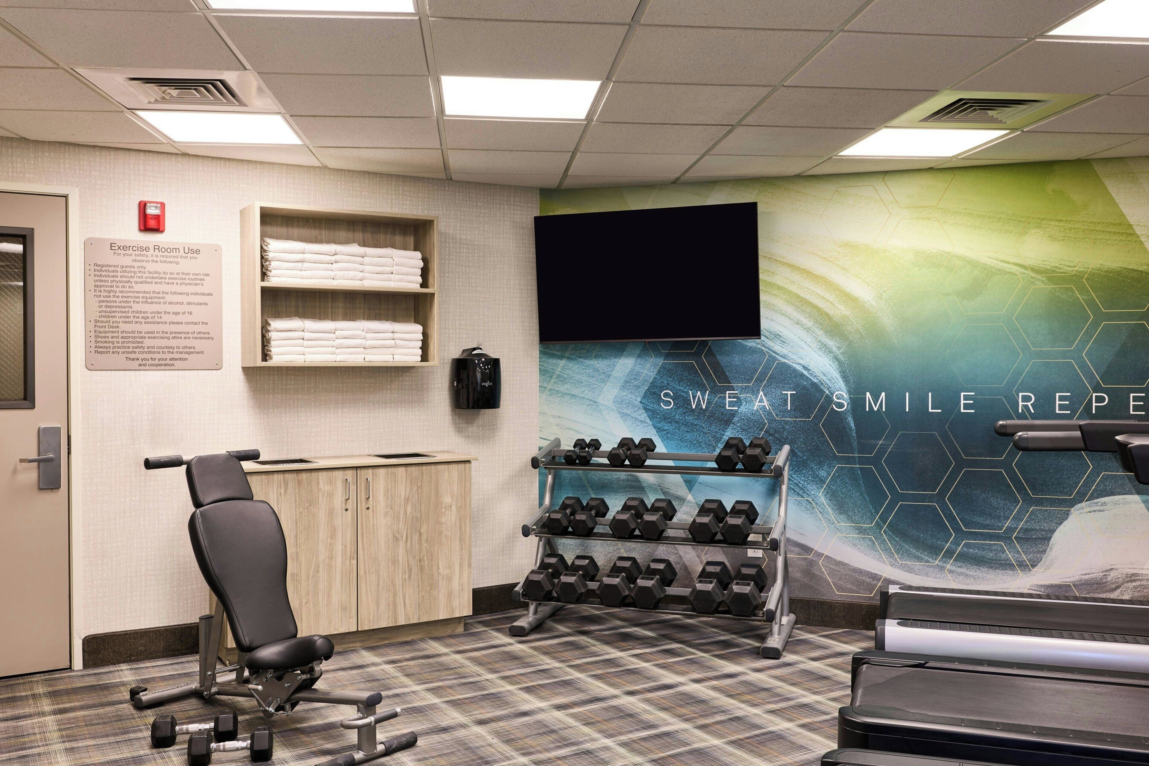 An exercise room with a treadmill, dumbbells, and a wall-mounted TV.
