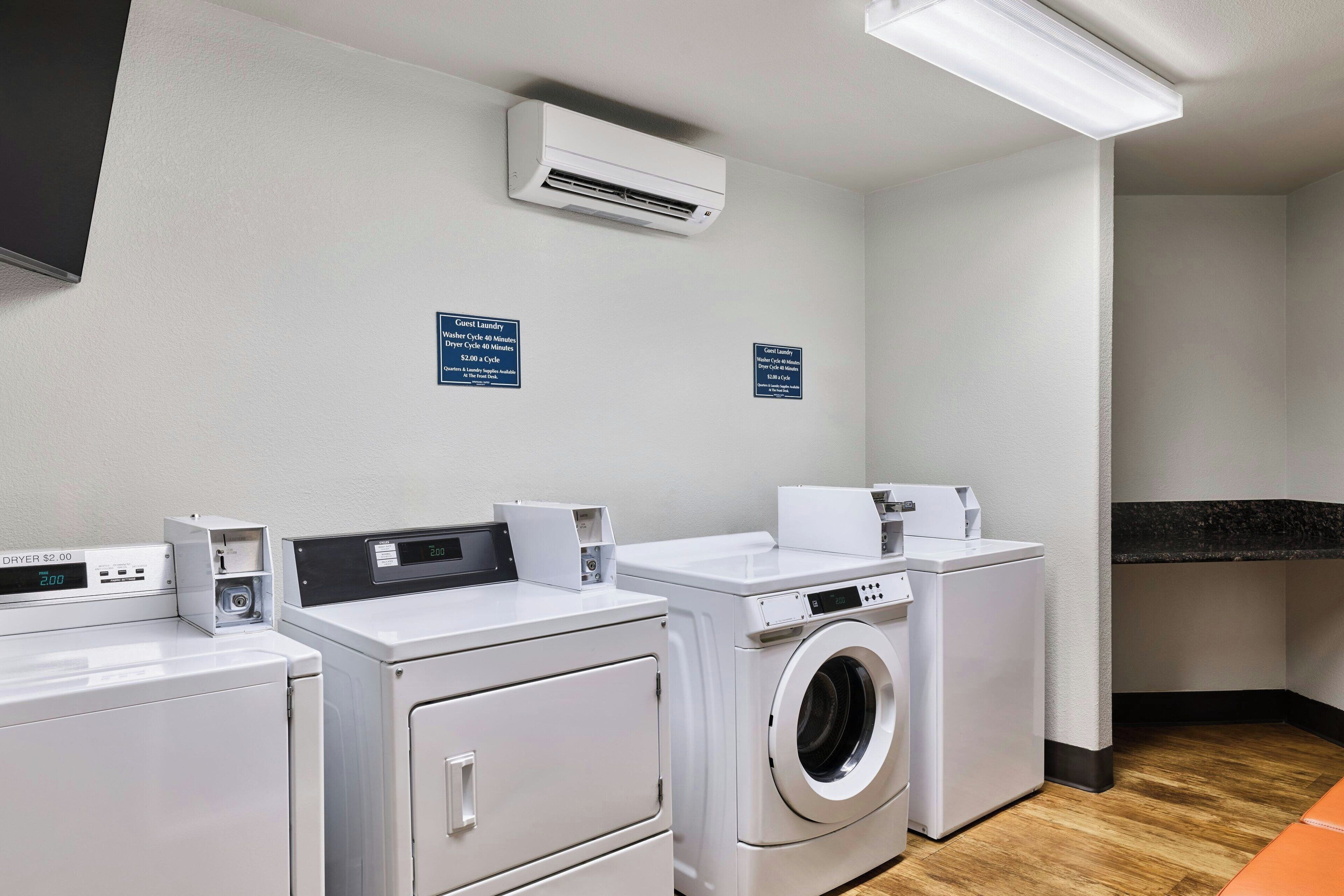 A laundry room with a dryer, washing machine, and a sign indicating guest laundry services.