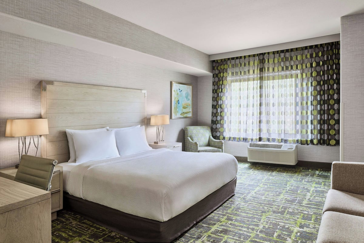 A hotel room with a large bed, two bedside lamps, a chair, a desk, and a window with curtains.