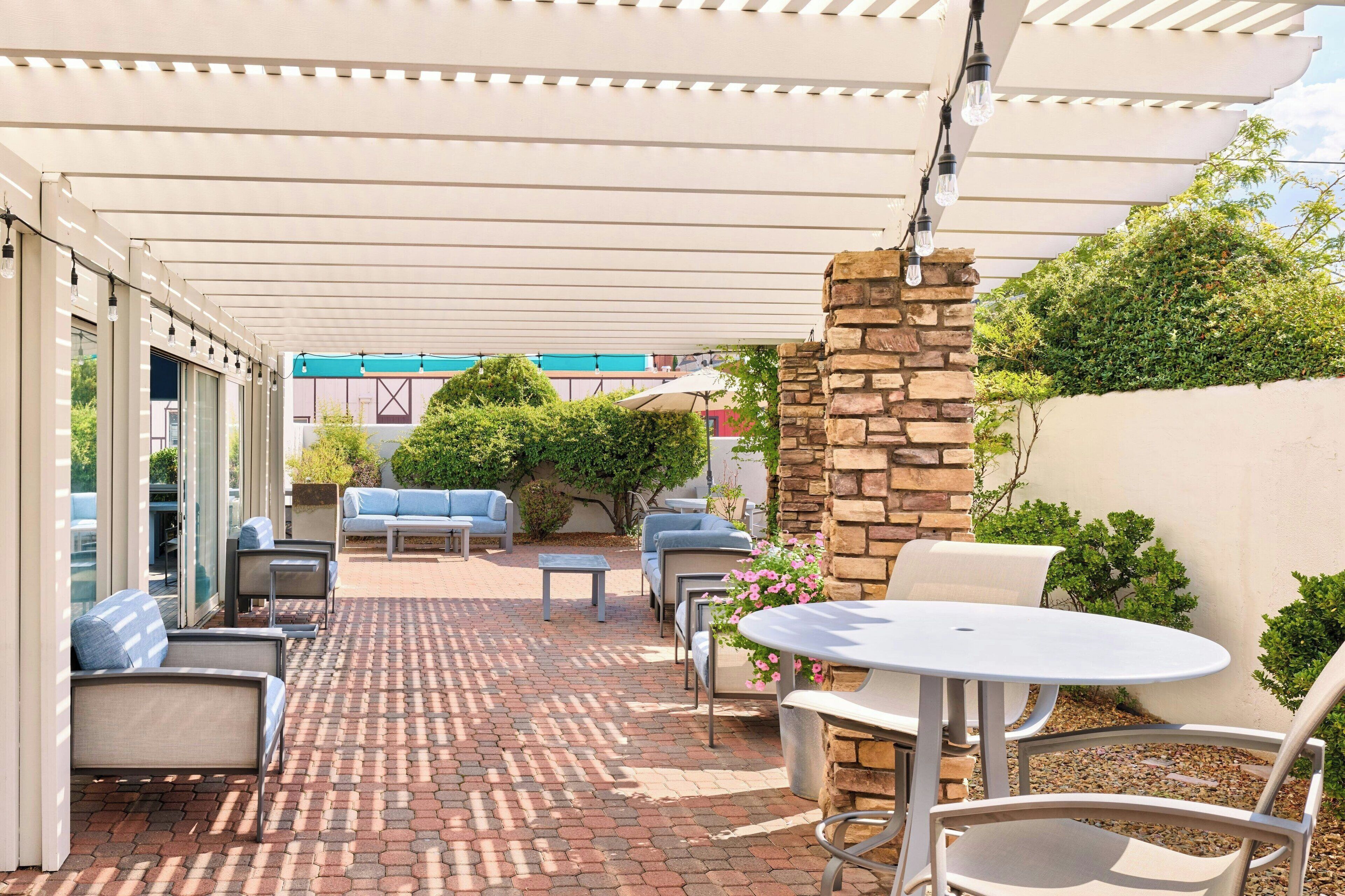 Un patio couvert avec un espace salon extérieur comprenant des chaises et une table, ainsi qu’un mur en pierre agrémenté de verdure.